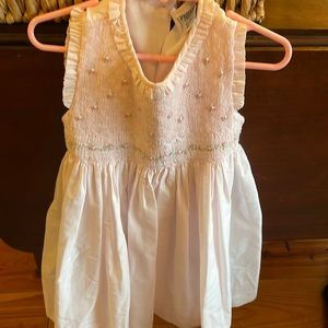 Pale pink smocked dress with flower detail and tie back.